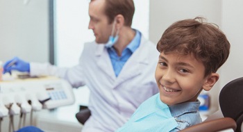 A young boy sitting in the dentist chair smiling while his dentist looks on