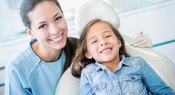 Young girl in dental chair and dental assistant smiling