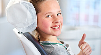 Young girl in dental chair gives thumbs up