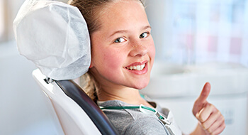 Young girl in dental chair gives thumbs up