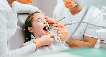 Dentist and assistant work on young sleeping patient