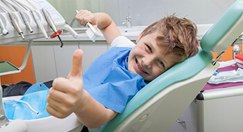Smiling boy in dental chair giving thumbs up