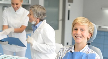 A teenage boy in the dentist’s chair while the dentist and dental assistant review a document