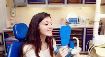 A young female looks at her smile in the mirror at the dentist’s office