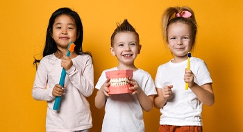 Three small children holding big toothbrushes and a mold of a mouth